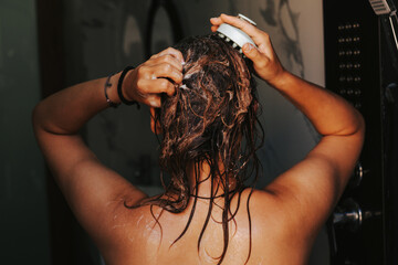 Naklejka premium Woman washes her hair with shampoo and massages head with a hair growth brush. Concept of hair care and the use of conditioner and mask to moisturize