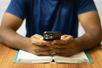 Young man using mobile phone keeping book as well on the table, taking notes in the mobile. Mobile phone addiction, man using mobile phone at night sparing his sleep, social media addiction