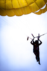 Person in silhouette parasailing with a yellow parasail in the sky