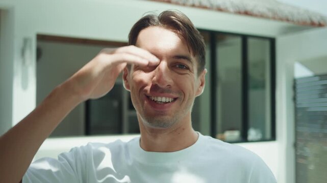 A smiling millennial man looks at the sun, covers his face with his hand, and then looks at the camera with a smile on his face. Concept of a happy smiling man. Millennial man, 35 years old.