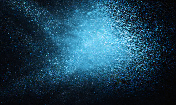 Abstract blue particles exploding in dark space with light glow dust explosion