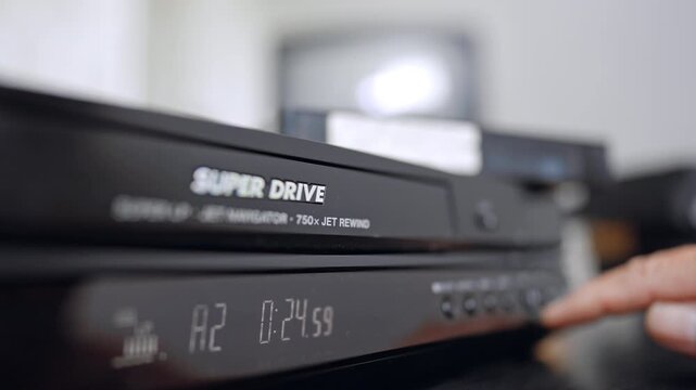 Front panel of the old VHS player. Close up. Hand presses the button on the recorder. Blurred backdrop.