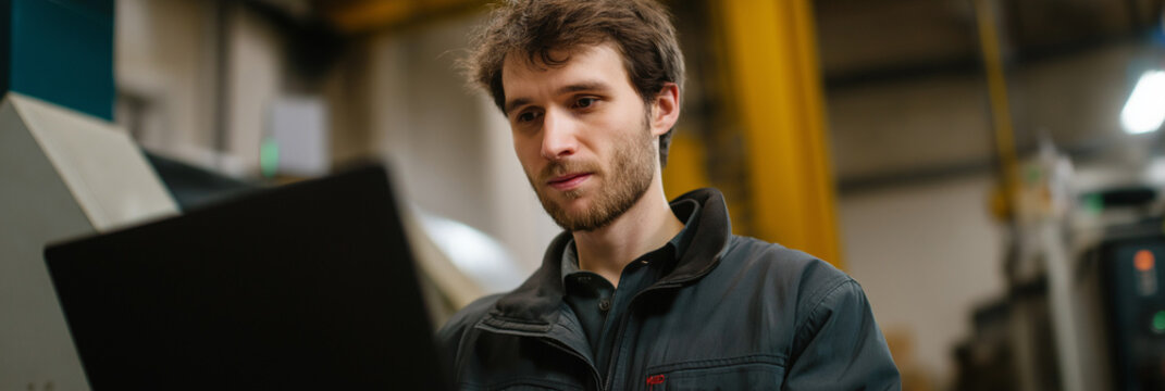 A diligent worker attentively analyzes data on a laptop in an industrial setting, highlighting concentration and the importance of technology in the modern workspace for productivity.