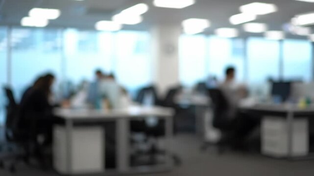 Blurred Office Space - The video shows a blurred office environment with employees working at their desks. The modern space is bright with natural light coming from the windows.