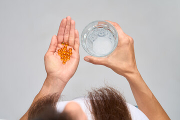 Top view of woman holding glass of water and omega-3 capsules 