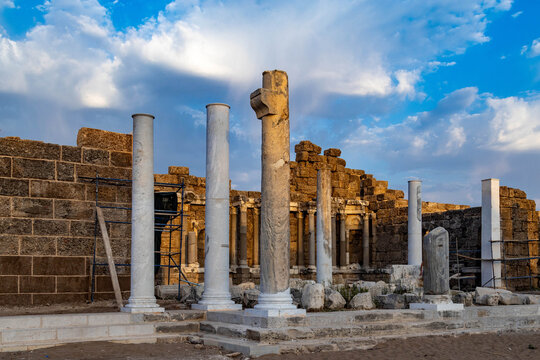 Ancient Roman ruins in old town Side with massive rusticated stone walls and partially destroyed Corinthian columns illuminated by warm pre-sunset light under blue sky. Turkey.

