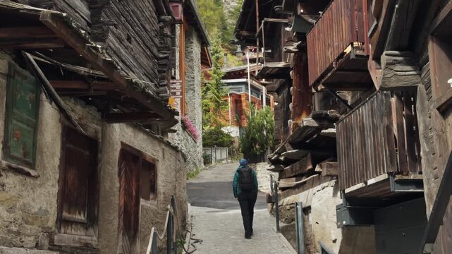 Tourist woman walking between old wooden houses in the historic village of Zermatt, Switzerland. Footage highlighting traditional architecture, alpine charm, and cultural heritage