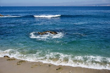 Turquoise Pacific waves breaking over sand and shoreline rocks near Cannery Row on Monterey Bay, California