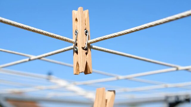 Clothesline with Wooden Clothespins Against Blue Sky - This video features a close-up of a wooden clothespin attached to a white rope clothesline.
