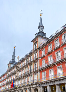 The highly decorated facade of Madrid's Casa de la Panader&iacute;a on the Plaza Mayor, featuring vibrant frescoes, two ornate towers, multiple balconies, and flags flying