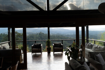 balcony or terrace with two wicker chairs and a potted plant, overlooking a mountainous landscape.