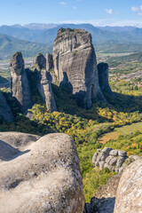 Vertical View of Towering Sandstone Pillars in Meteora, Greece, Framed by Textured Foreground Rocks, with the Thessaly Valley in the Distance