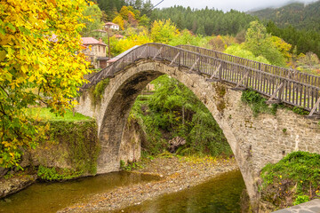 Low-Angle View of the Historic Single-Arch Stone Bridge Over the Dried Aoos Riverbed in Vovousa Village, Pindos, Greece, During Autumn