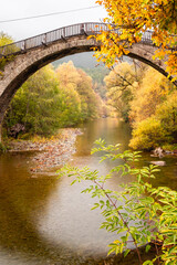 Vertical View of the Historic Stone Bridge and Traditional Houses of Vovousa Village, Pindos, Greece, During a Colorful Autumn Day
