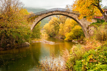 Iconic Single-Arch Stone Bridge of Vovousa Village Spanning the Aoos River, Surrounded by Golden Autumn Foliage in Pindos, Greece