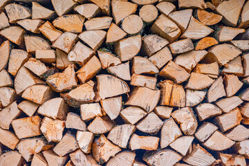 Full Frame Close-up of a Neatly Stacked Wall of Split Firewood, Showing the Textured Wood Grain and Natural Light Brown and Orange Tones