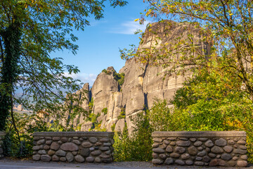 View of the Towering Sandstone Rock Formations of Meteora, Greece, Framed by Trees and a Traditional Stone Boundary Wall