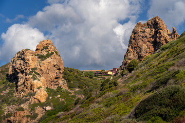 Orange, red, massive, and fractured rocks, covered with Mediterranean shrubs in Nebida, Sardinia (Italy). Geological formation consisting of quartzite and sandstone.