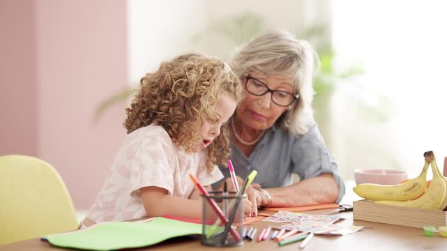 Caring grandmother teaching granddaughter how to draw at home