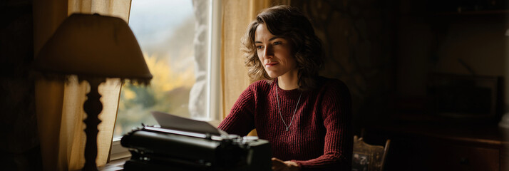 A contemplative woman sitting by a window, engaged in typing on a vintage typewriter, illustrating the beauty of creativity and reflection in a serene environment.