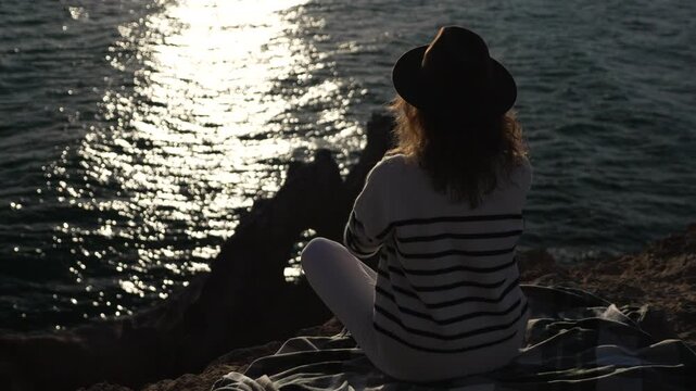 Woman meditation ocean, contemplative figure sitting on cliff edge practicing yoga during glowing sunset travel lifestyle.