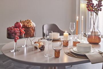 Beautifully decorated tablescape for a holiday dinner. Close-up on decor details like fruits (grapes, pomegranate), pumpkins, and a reindeer figure. Warm, cozy ambiance.