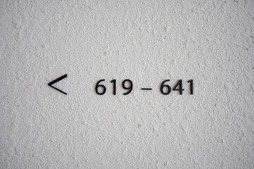 Minimalist black signage on a textured white wall indicating room numbers 619–641 and an arrow pointing to the left.