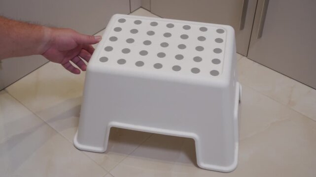 Grating Scrape: Hand Slides White Plastic Step Stool Across Tiled Floor.