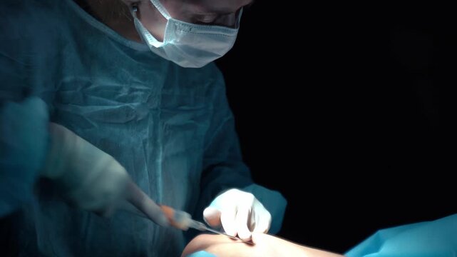 Professional surgeon in a dark operating room carefully performing a lipofilling procedure, harvesting fat cells with a cannula and syringe for cosmetic body contouring and augmentation