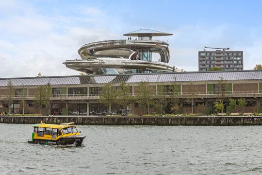 A unique modern structure on the Fenix I warehouse in Rotterdam, housing the Fenix Museum of Migration, with a yellow water taxi passing on the river. Rotterdam, Netherlands. 19 October 2025.
