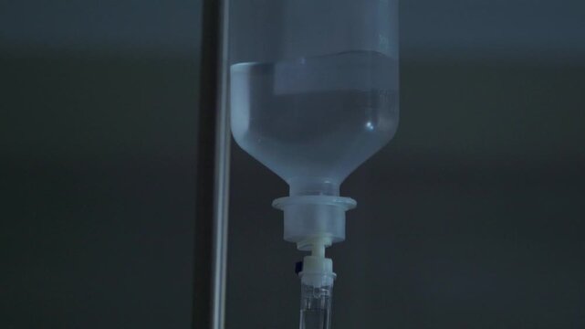 Close up of an intravenous drip bag hanging on a metal pole, with saline solution flowing into a tube for medical treatment in a hospital room, illustrating healthcare and recovery concepts