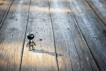 Small silver astronaut figurine standing on wooden floor, illuminated by sunlight, concept of exploration, curiosity, and dreams of space in a minimalist setting