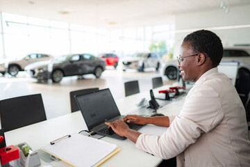 Smiling saleswoman using laptop in car dealership