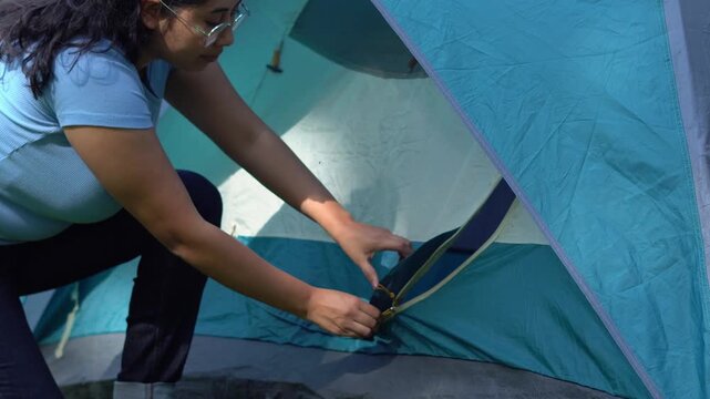 A young woman kneels outside her tent, unzipping the entrance to step in, surrounded by morning light and peaceful forest air.