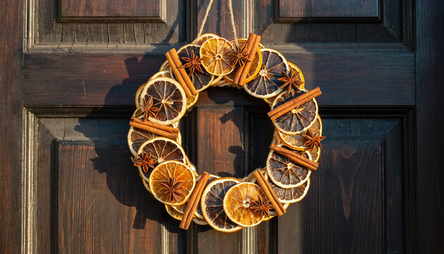 A fragrant dried citrus and cinnamon stick wreath hangs on a rustic wooden door. - Powered by Adobe