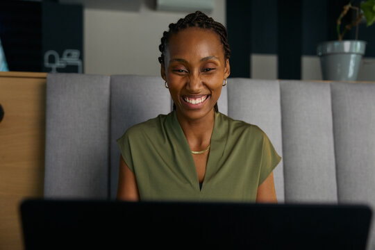 Smiling young black businesswoman using laptop at desk in office lobby during workday