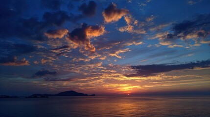 Naklejka premium A stunning sunset casts warm colors across the sky, reflecting on the calm ocean waters. Distant islands create a serene backdrop as day transitions to night.