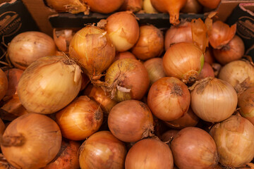 Fresh yellow onions with dry skins piled in box at vegetable market. The natural colors, light, and texture highlight freshness and simplicity of local produce.