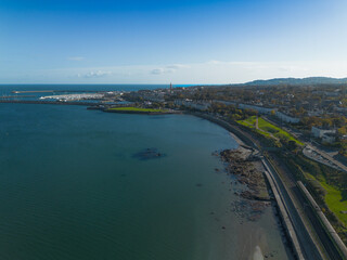 A beautiful blue ocean with a city in the background. The city is full of buildings and mountains in the background. railway tracks along the sea coastline. Dublin south view, Blackrock