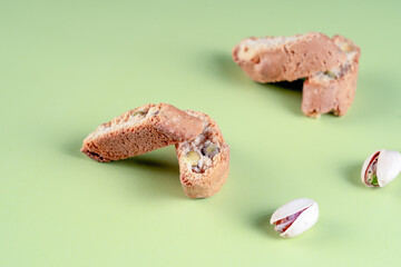 Authentic Italian almond biscotti, enriched with green pistachios, presented on a light green background with scattered nuts