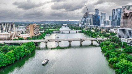 Panoramic aerial shot of Austin, Texas. The Colorado River flows beneath a bridge with city skyscrapers in the background under dramatic cloudy skies. Modern urban landscape, river views, Texas.