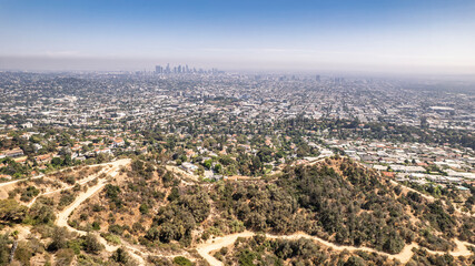 Drone shot of Griffith Observatory perched atop a hill with expansive Los Angeles city view. Dry vegetation, winding path, bright blue sky, urban sprawl, California landscape, iconic landmark