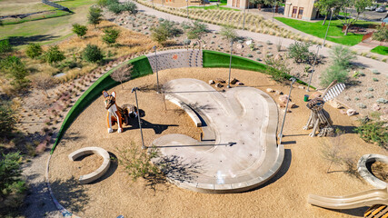 Drone shot of a modern skate park in Arizona. Kids playing, concrete ramps, sandpit, green landscaping. Great for recreation, youth, family, urban design.
