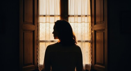 Female adult silhouette looking out a vintage window. Cinematic scene with warm golden hour sunlight. Concept of introspection and personal reflection