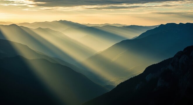 Majestic mountain range with golden sunbeams breaking through clouds. Layered mountain silhouettes in morning haze. Inspirational concept for hope vision and new opportunity