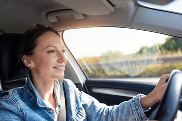 Portrait young adult happy smiling woman in sunglasses drives sunny highway road wearing denim jacket. Light reflects face enjoys relaxed travel trip moment countryside bright spring summer weather