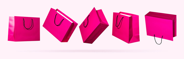 Set of bright pink glossy paper shopping bags with black rope handles flying from different sides on light pastel background. Concept of women fashion shopping, retail sales, seasonal promotions