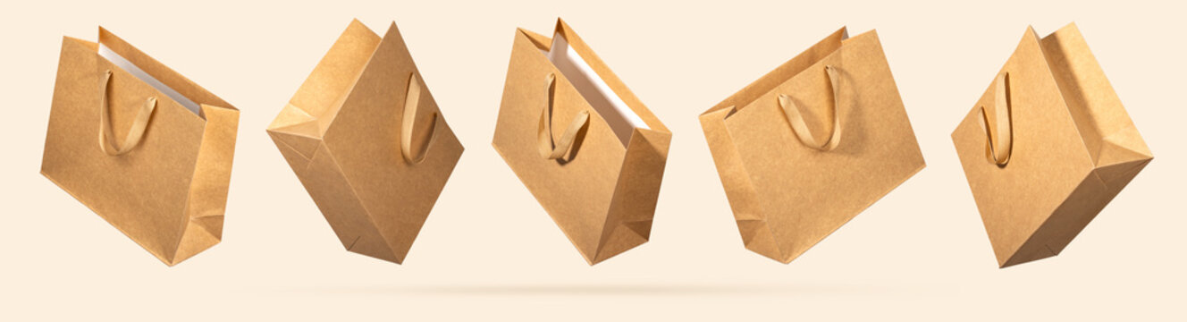 Five kraft paper shopping bags flying on beige background. Concept of eco-friendly packaging design for conscious retail, marketing visuals and sustainable shopping concepts. Mockup for branding