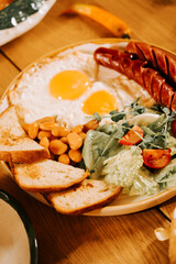 Breakfast plate with eggs, sausages, beans, salad, and bread on a wooden table