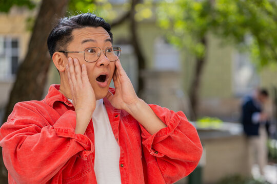 Oh my God, Wow. Asian middle-aged man looking surprised at camera with big open eyes shocked by victory game winning, lottery goal achievement, good news outdoors. Chinese guy on urban city street